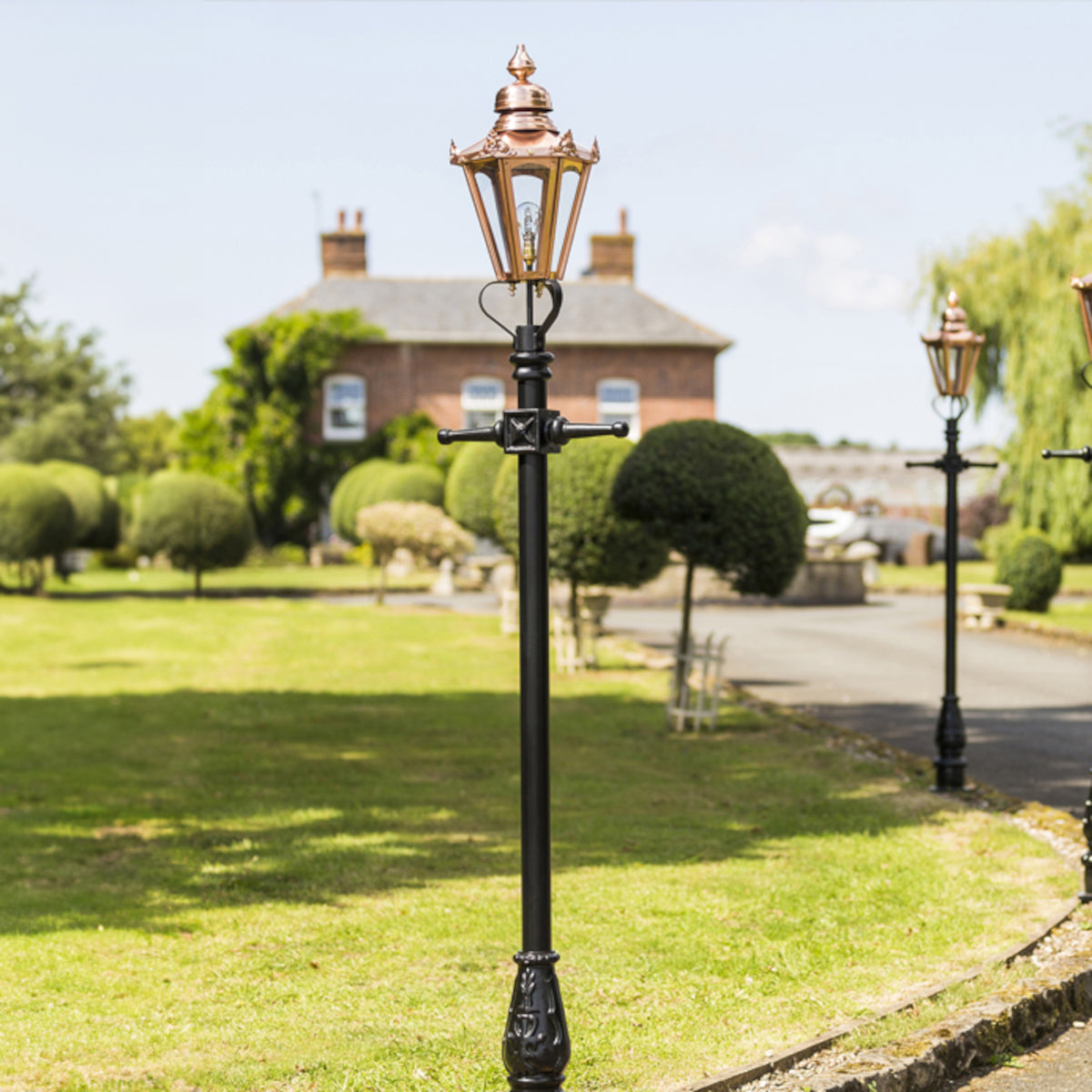 Three copper lamp posts lined up on a driveway